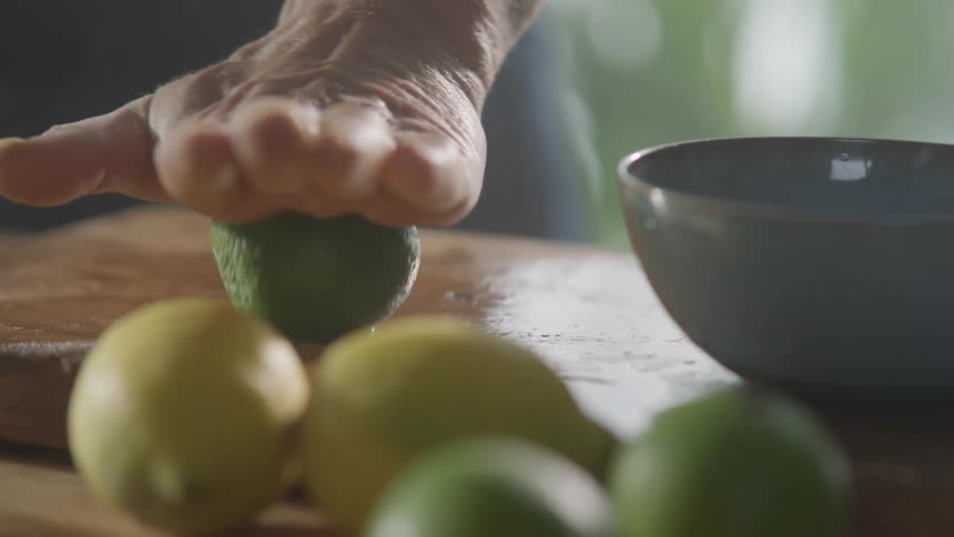 A mans hand rolls a lime on a cutting board before cutting it in the kitchen