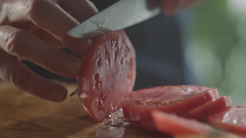 Man uses a very sharp kitchen knife to slice tomatoes on a cutting board in the kitchen