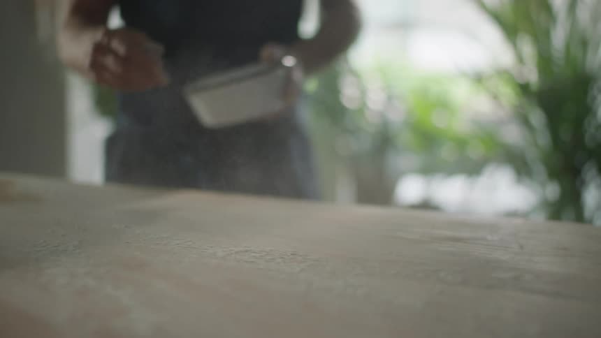 A man throws flour on to a wood top counter surface
