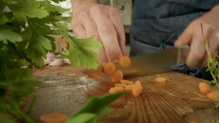 Cook cuts carrot with a knife on a cutting board in the kitchen