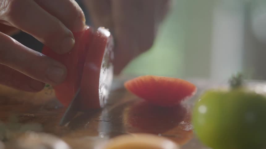 A white person cuts a tomato with a knife
