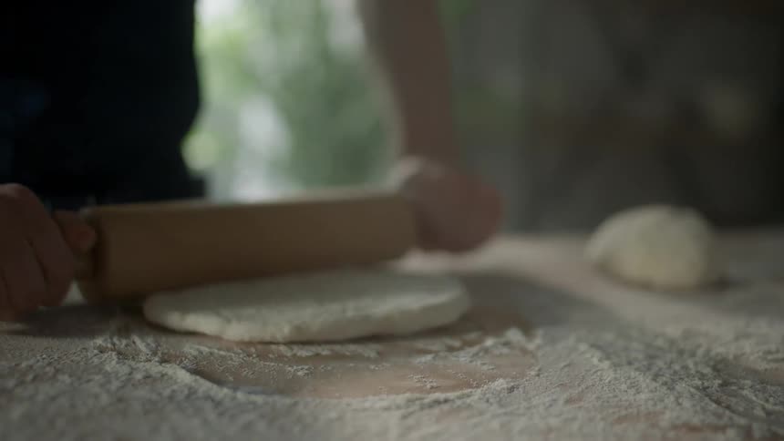 Man with a black shirt rolls out dough in the kitchen