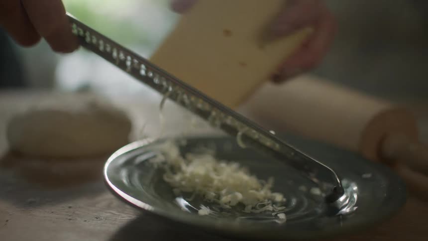 Man grates cheese into a plate in kitchen