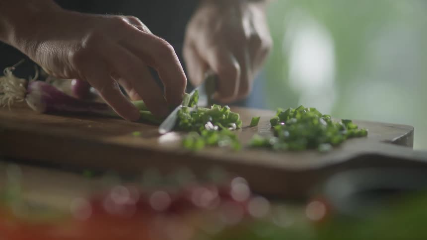 A person uses a knife to chop fresh herbs on a cutting board
