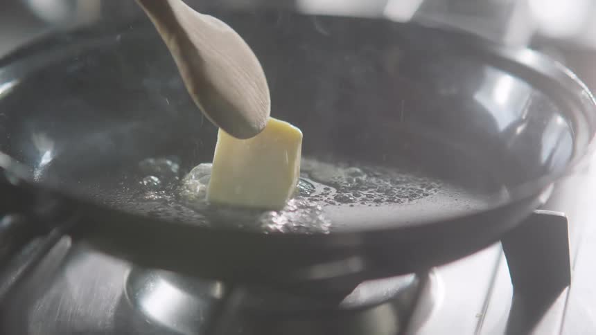 A wooden spoon spreading butter in a frying pan on a stove