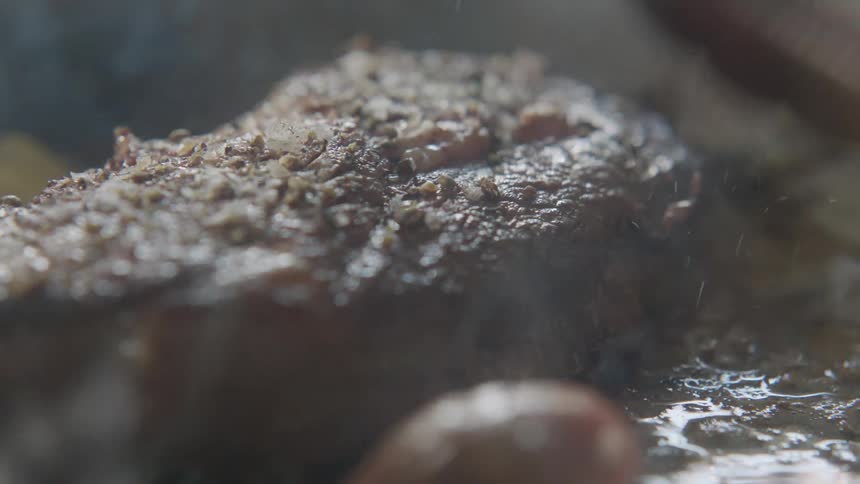 A person is cooking steak on the grill