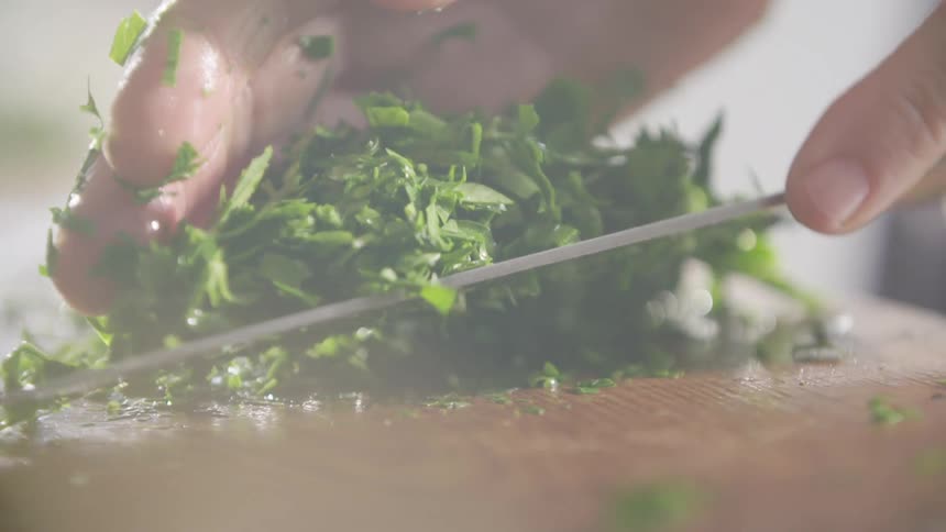 A white male uses a knife and a hand to scoop up cut greens in a kitchen