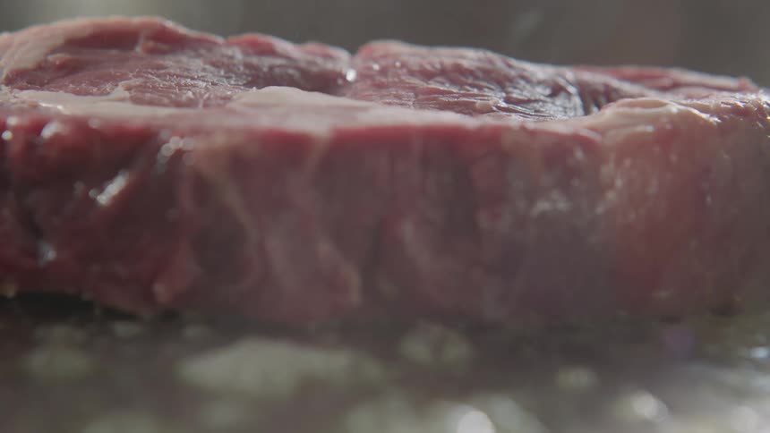 Thick piece of steak being placed on a sizzling pan