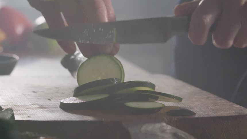 Man uses a sharp kitchen knife to slice a cucumber on a cutting board