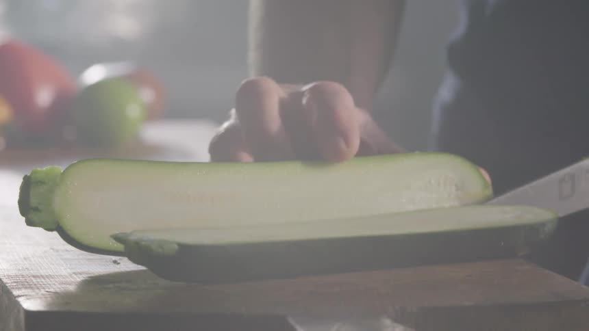 Zucchini falls into two pieces on chopping board after person slices it with knife