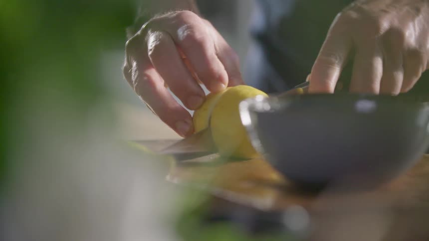 Man cuts a yellow lemon with a sharp knife on a cutting board in the kitchen