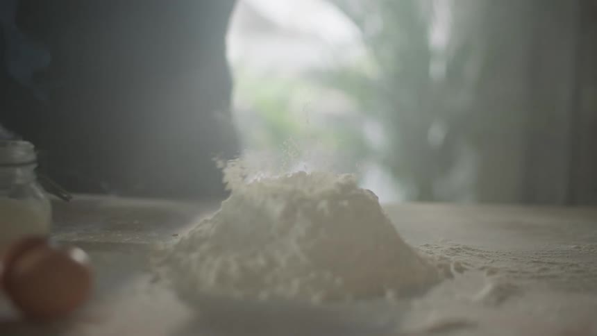 A person drops an egg yolk into a pile of flour