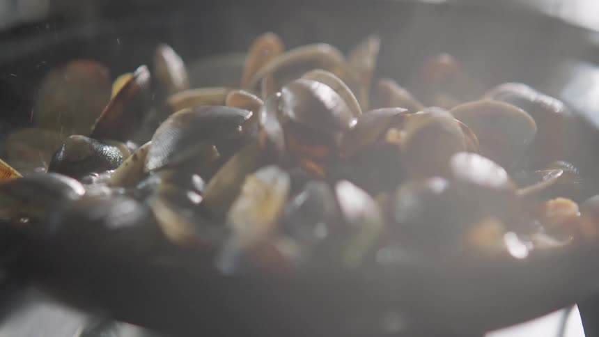 Clams stewing and smoking in a pan over a stove