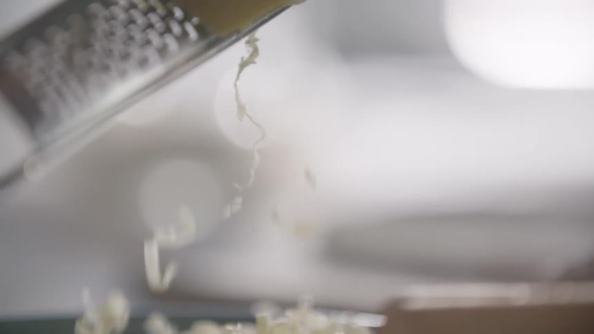 Man grates cheese into a plate in the kitchen