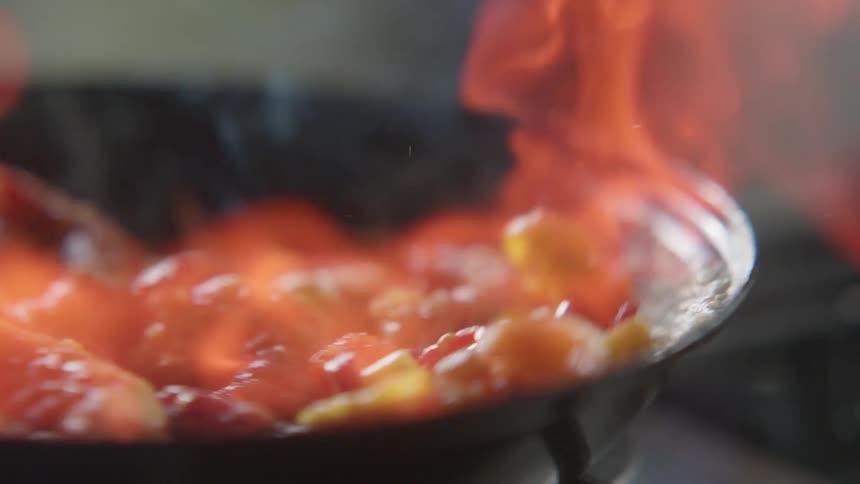 Shrimp and vegetables cooking on a frying pan on fire over a stove