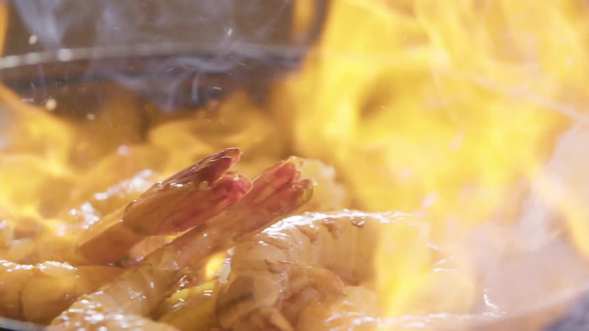Pouring alcohol on shrimp while flambeing in a skillet