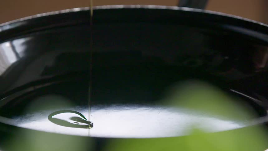 Cooking oil being poured in a black metal pan