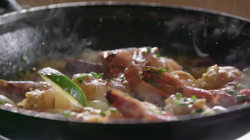 Narrow lime wedges are dropped into skillet onto tail on shrimp