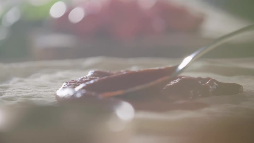 A spoon spreading tomato sauce on dough
