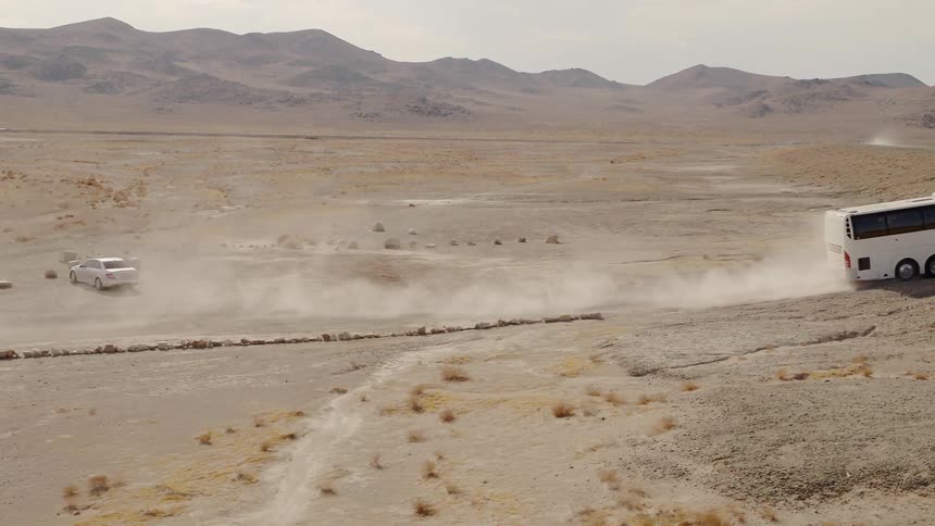 Tour bus drives on a dirt road through the desert