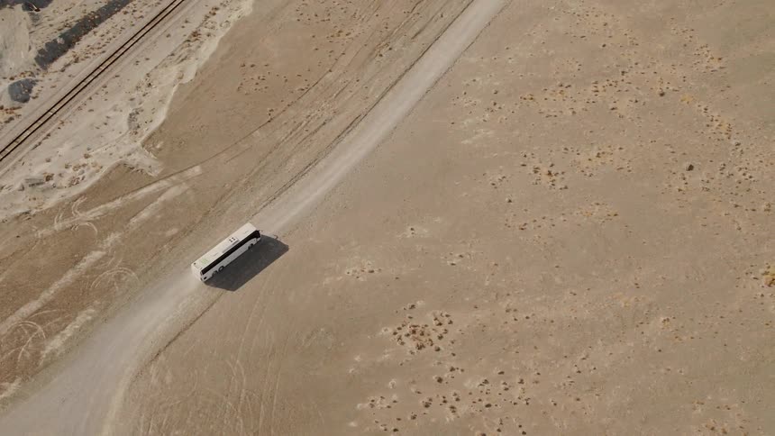 Aerial view of a white bus driving on a dirt road through dry plains