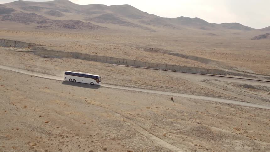 Charter tour bus drives along dirt road through barren desert