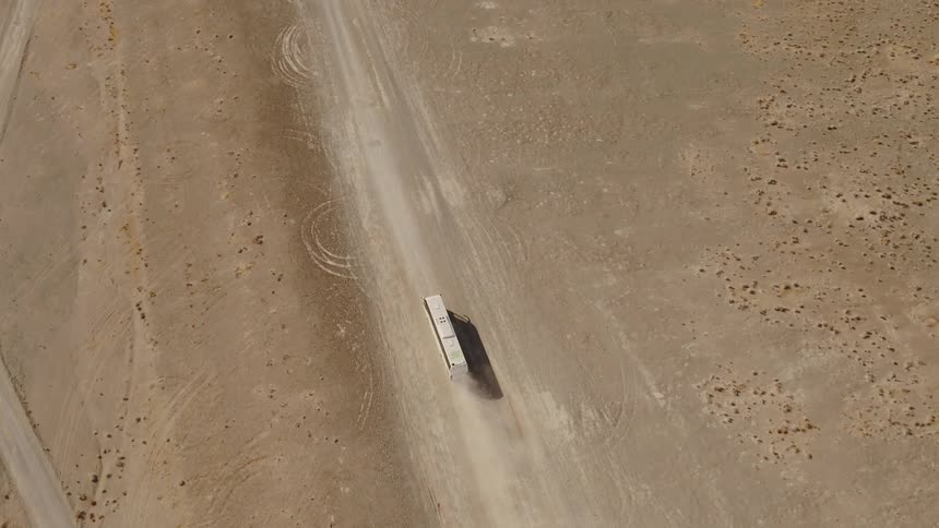 Aerial view of a white bus driving on a dirt road through the dry plains