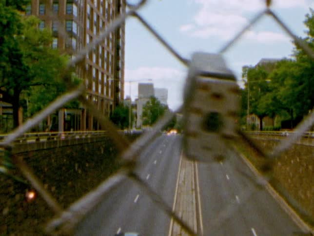 A chain link fence guards a pedestrian bridge that runs over a four lane road in a neighborhood near downtown