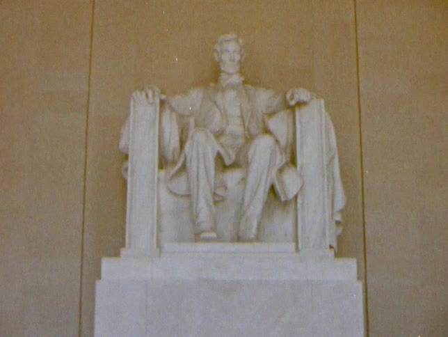 Lincoln memorial statue sits under words carved into wall