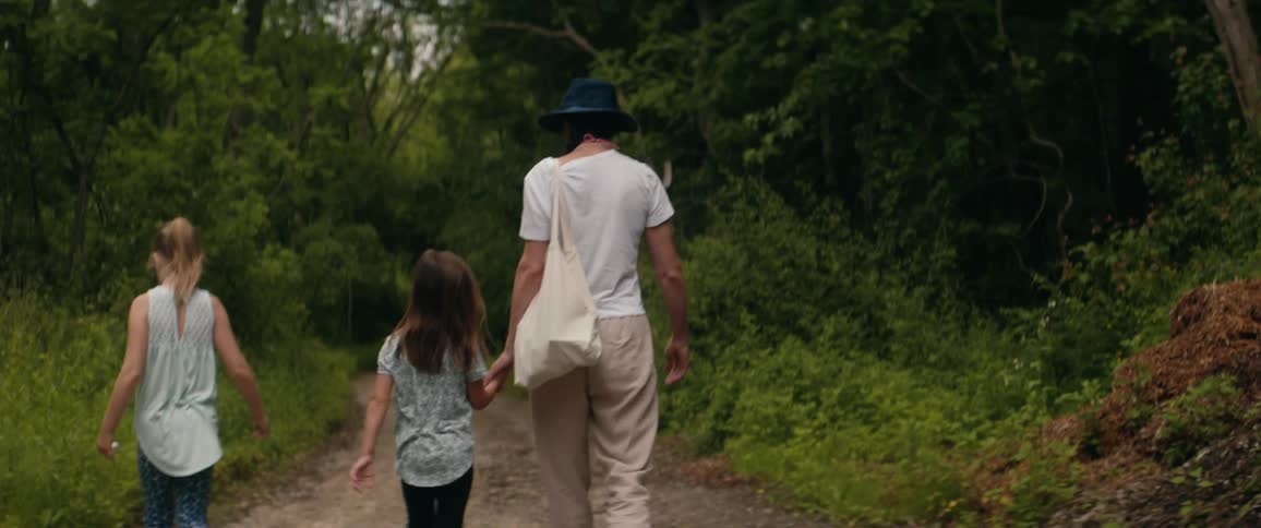 A mother walks with her two daughters down a path in a forest