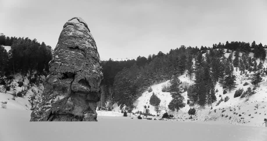 A large rock formation rises out of a snow covered plain