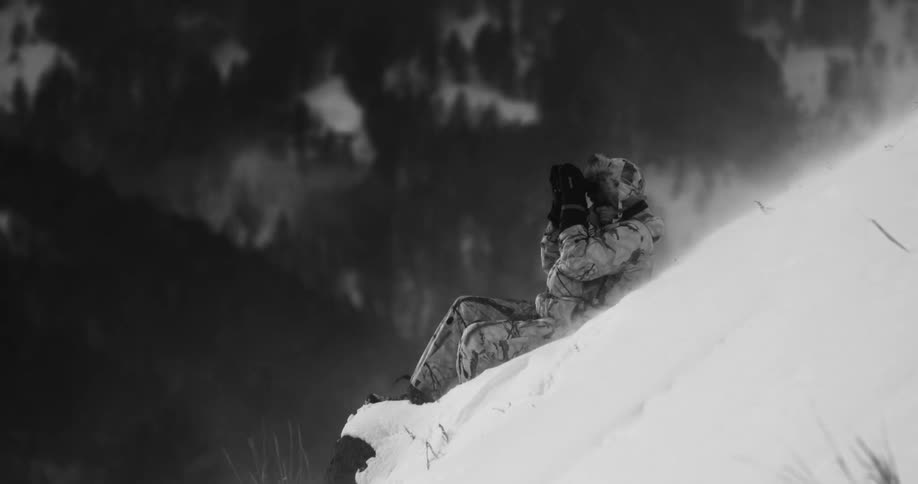 Hiker sits on the side of a snowy hill as the snow blows around him