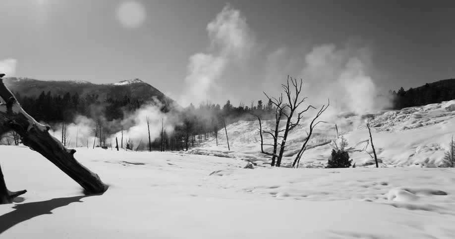 Clouds of vapor rise on the clear sky over the snow covered hills