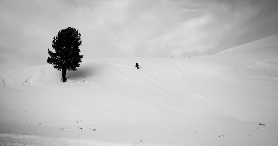Skier skis down a snowy hill under a cloudy sky