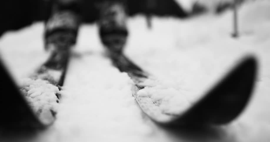 A person attaches skis to the bottom of their footwear before walking forward and out of frame