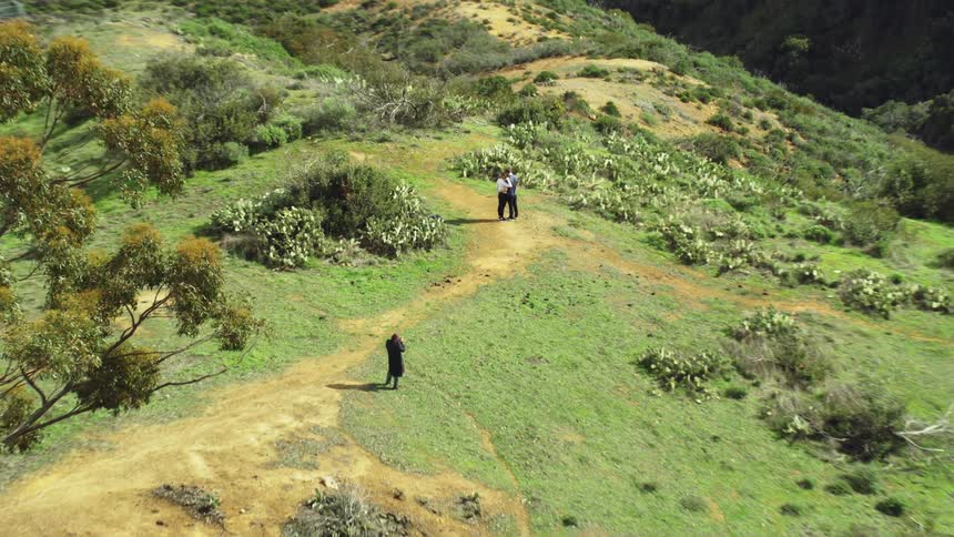 Two people hug with another watching on the mountain