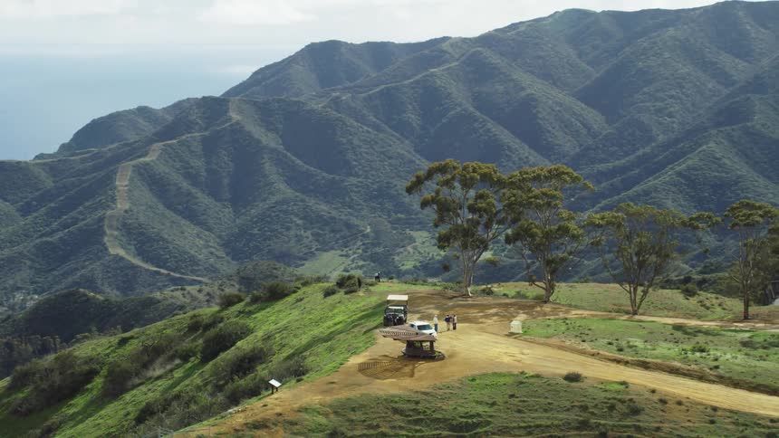 A small group of people and two vehicles are on a hillside mountain top