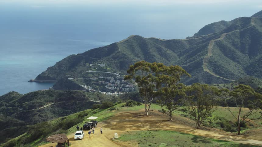 People stand next to their vehicles parked on a hilltop near the ocean