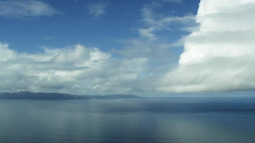 Aerial view of clouds over the calm ocean waters next to mountains in the coast line