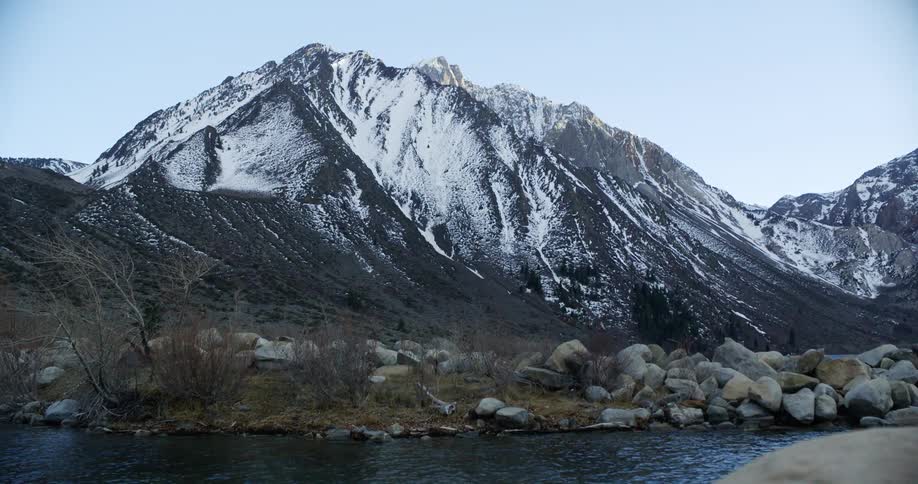 River winds past large snow covered mountains with shore dotted by large boulders