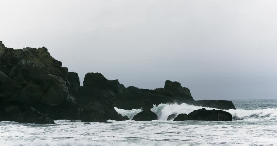 Waves crash against rocks on shore foaming and throwing up spray