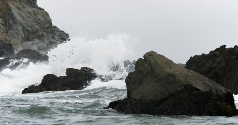 Ocean waves crash against big rocks on a cloudy day