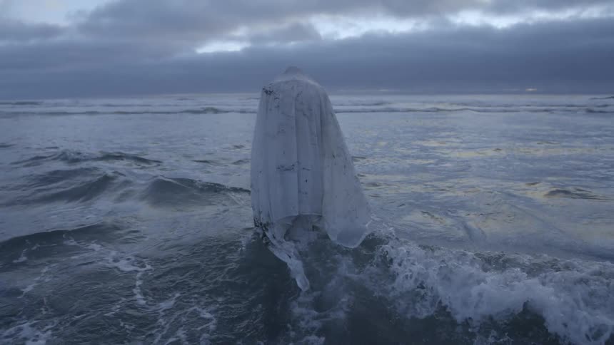 A person wrapped in a large white cloth walks into the ocean