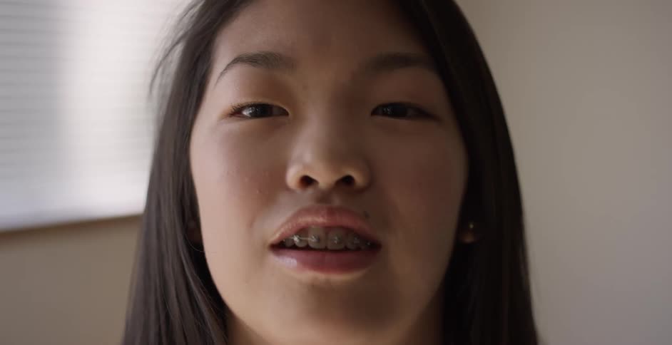 A young asian woman with braces talks and laughs while looking into the camera