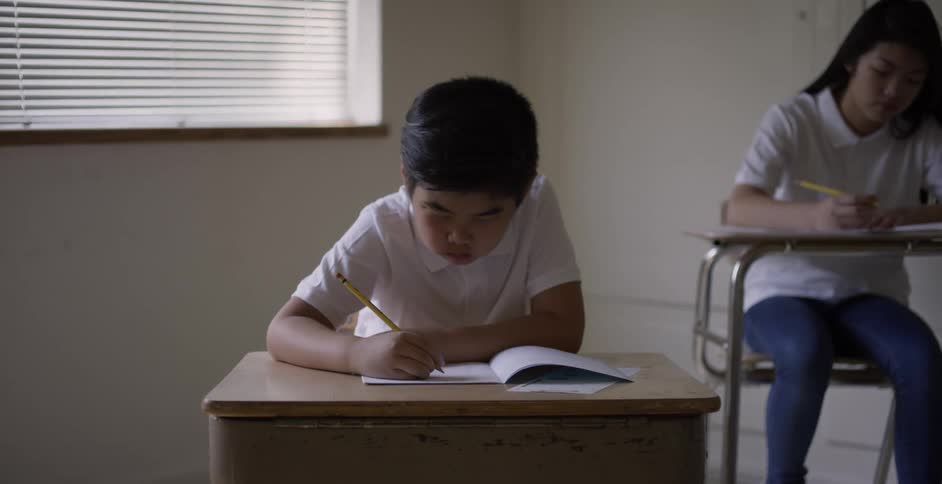A teacher walks around students writing at desks