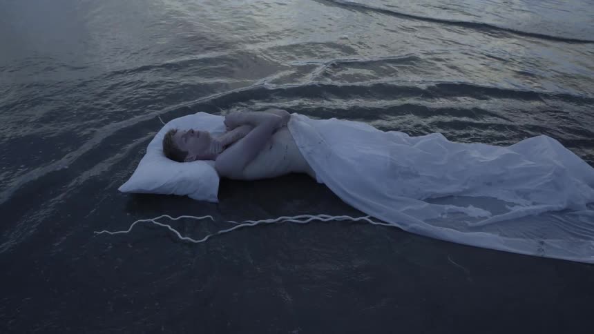 Man laying down on sand in ocean water with tarp