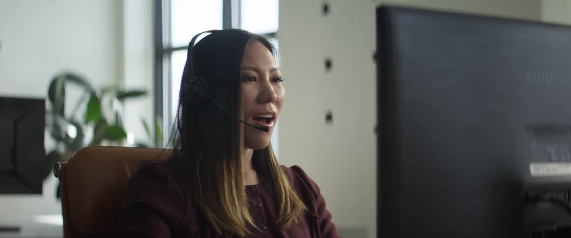 A woman in an office talks on the phone and uses her computer