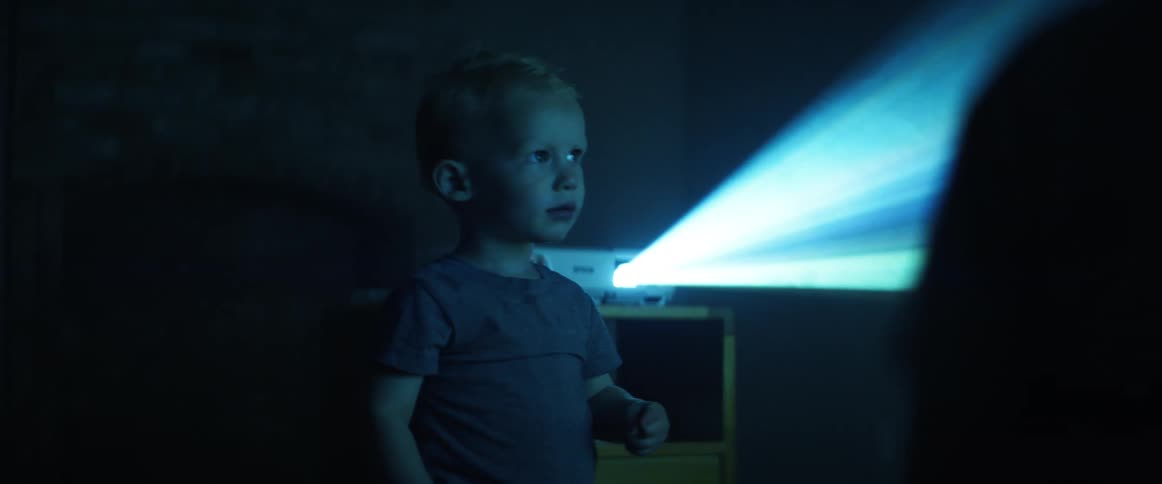 A young boy reacts and points while watching video from a projector