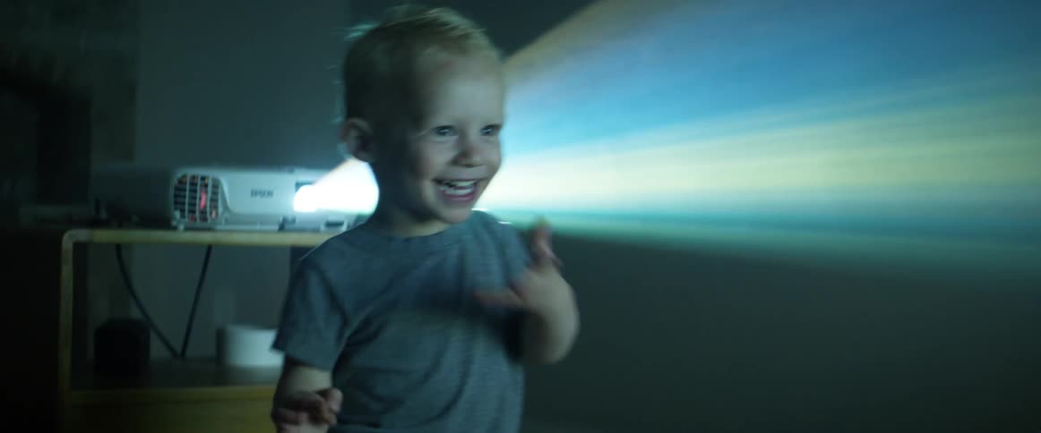 A little boy happily standing in the light of a projector in a dark room