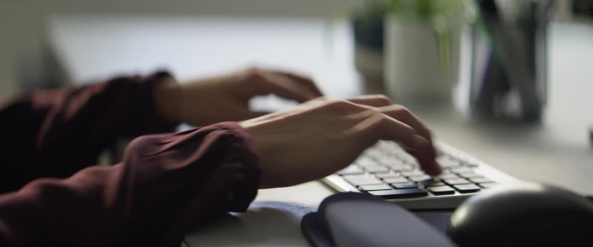 A person sitting at a desk typing on a computer keyboard during the day